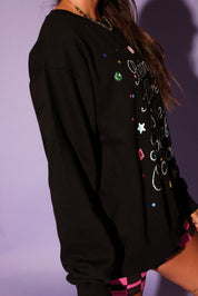 Black sweatshirt with colorful embellishments on a purple background, side view