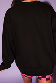 Person wearing a black oversized sweatshirt and checkered shorts against a purple background, back view