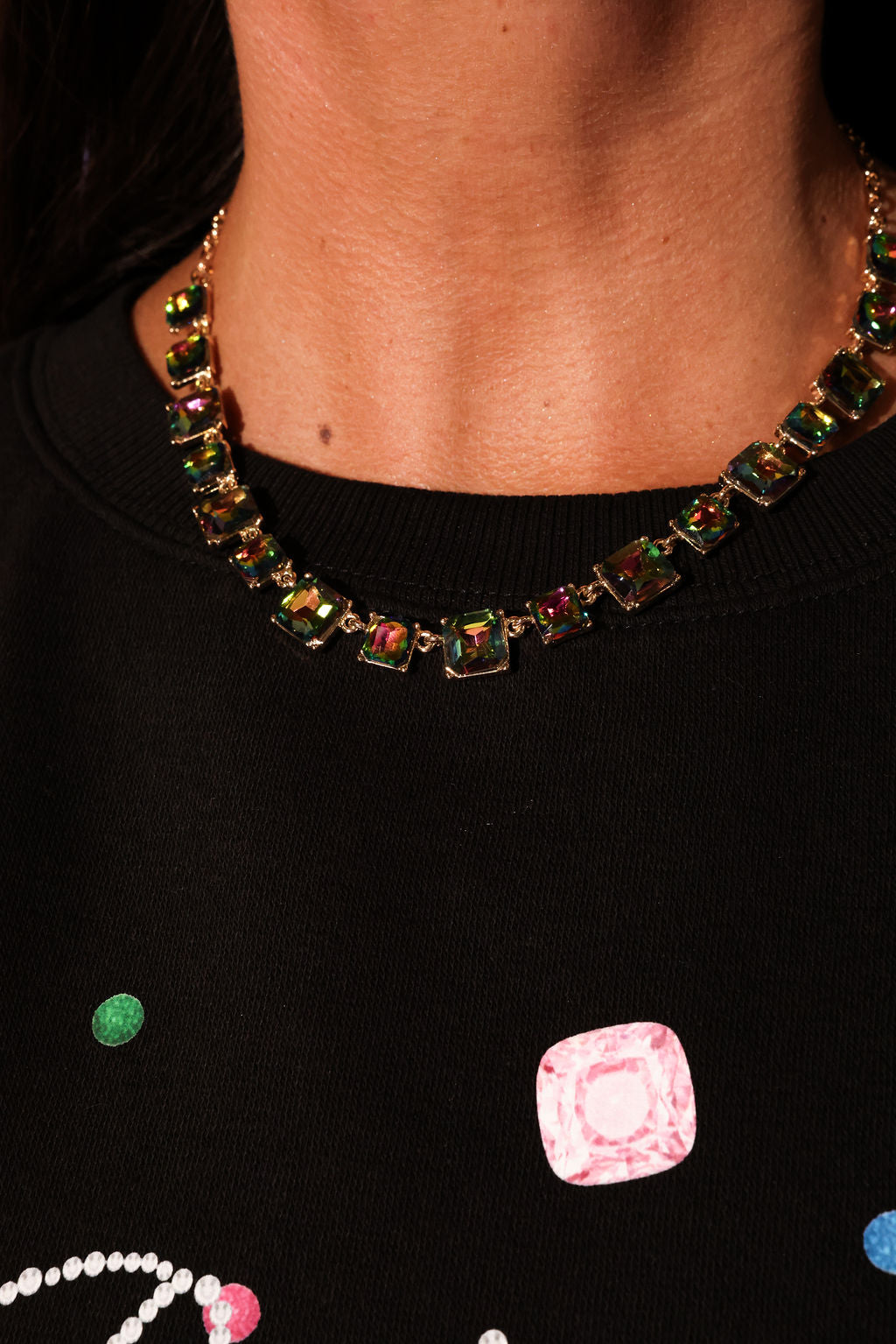 Necklace with multicolored gemstones worn by a person, with a black background featuring colorful square patterns