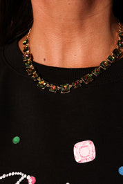 Necklace with multicolored gemstones worn by a person, with a black background featuring colorful square patterns