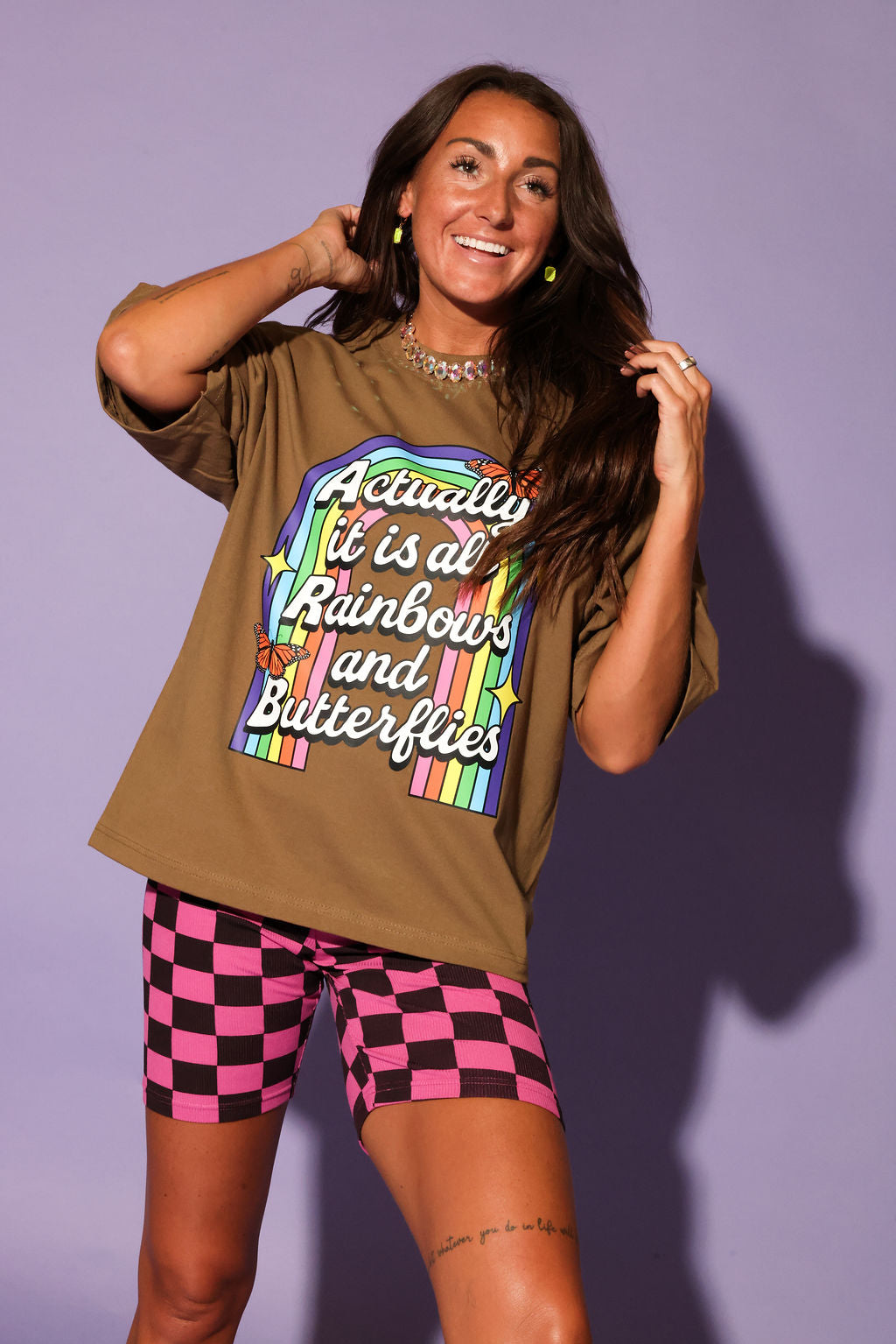 Woman wearing a graphic t-shirt with colorful text and checkered shorts against a purple background