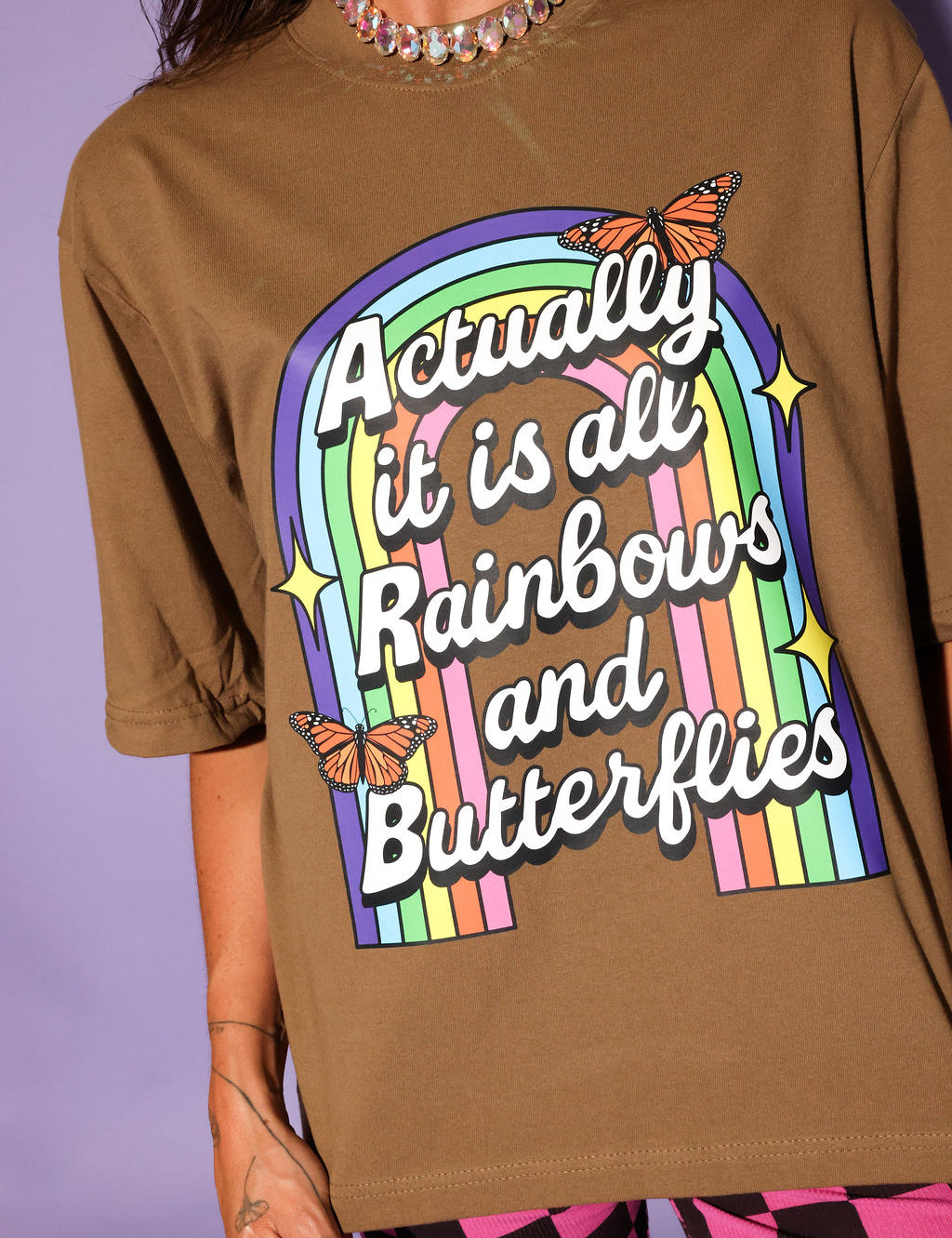 Brown t-shirt with rainbow and butterfly design on a purple background, close up frontal view