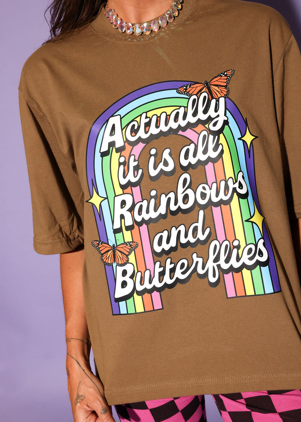 Brown t-shirt with rainbow and butterfly design on a purple background, close up frontal view