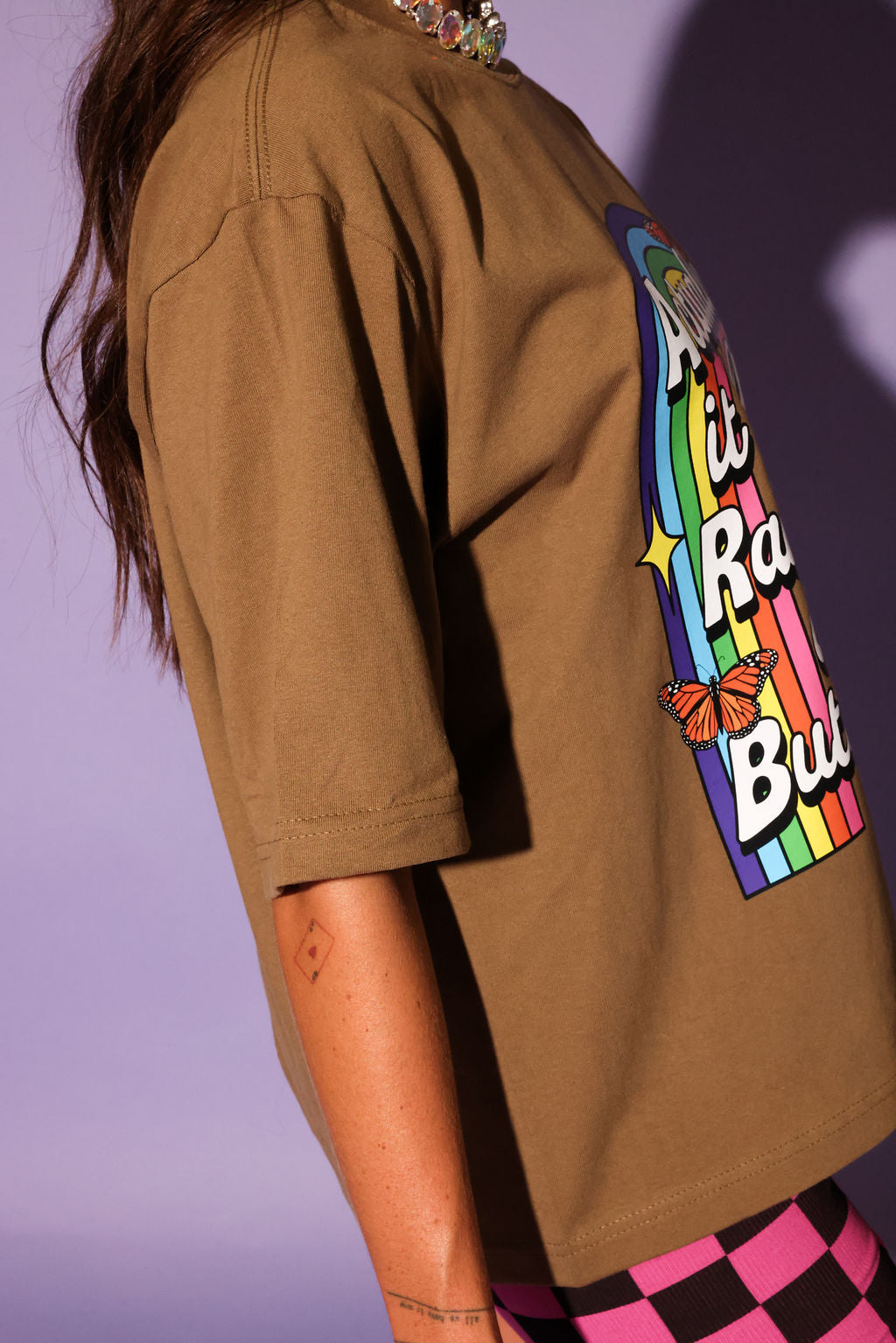 Person wearing a brown t-shirt with a colorful graphic design on a purple background, side view