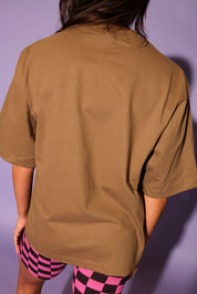 Person wearing a brown t-shirt and checkered shorts with pink and black pattern against a purple background, close up back view