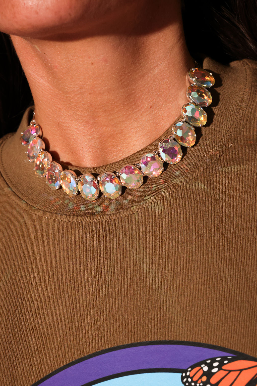 Close-up of a person wearing a colorful beaded necklace on a brown shirt with a butterfly design