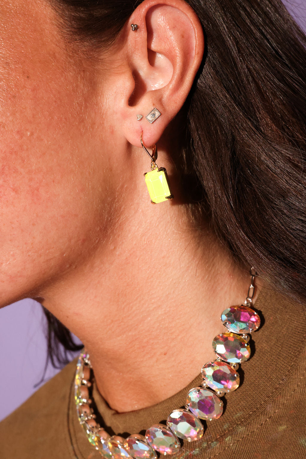 Close-up of an ear with a yellow earring and a colorful necklace against a purple background