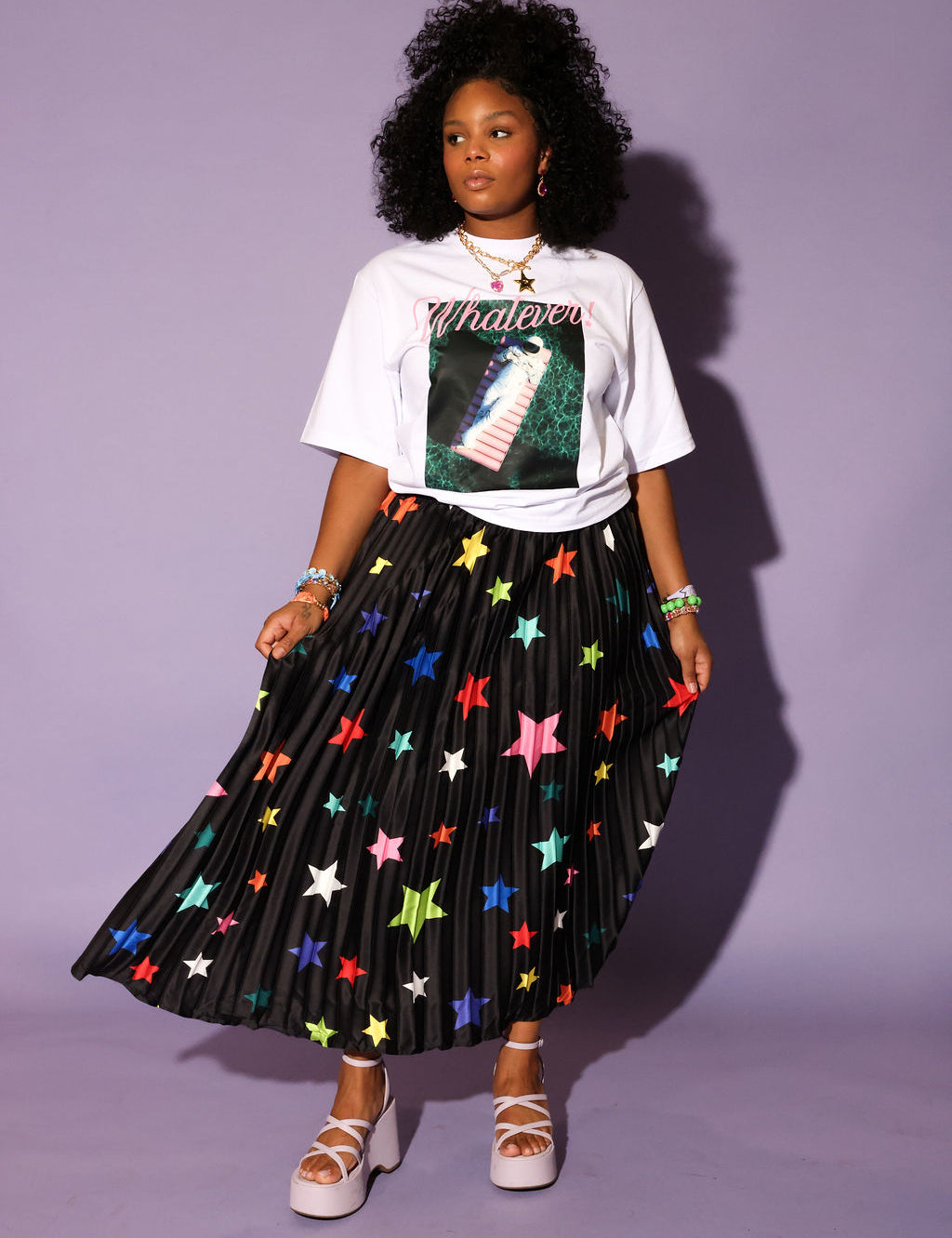 Woman wearing a graphic t-shirt and star-patterned skirt against a purple background, frontal view