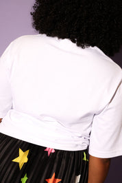 Person wearing a white shirt and a black skirt with colorful star patterns against a purple background, back view