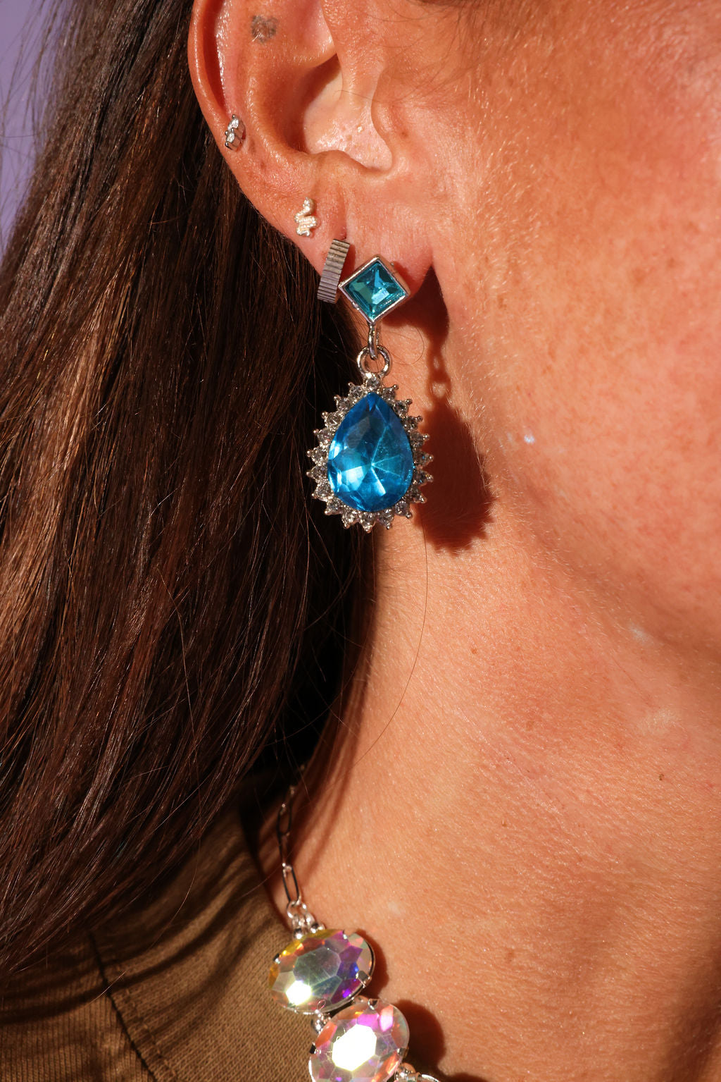 Close-up of a person wearing blue teardrop earrings with a blurred background