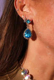 Close-up of a person wearing blue teardrop earrings with a blurred background
