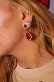 Close-up of a person wearing red and clear gemstone earrings.