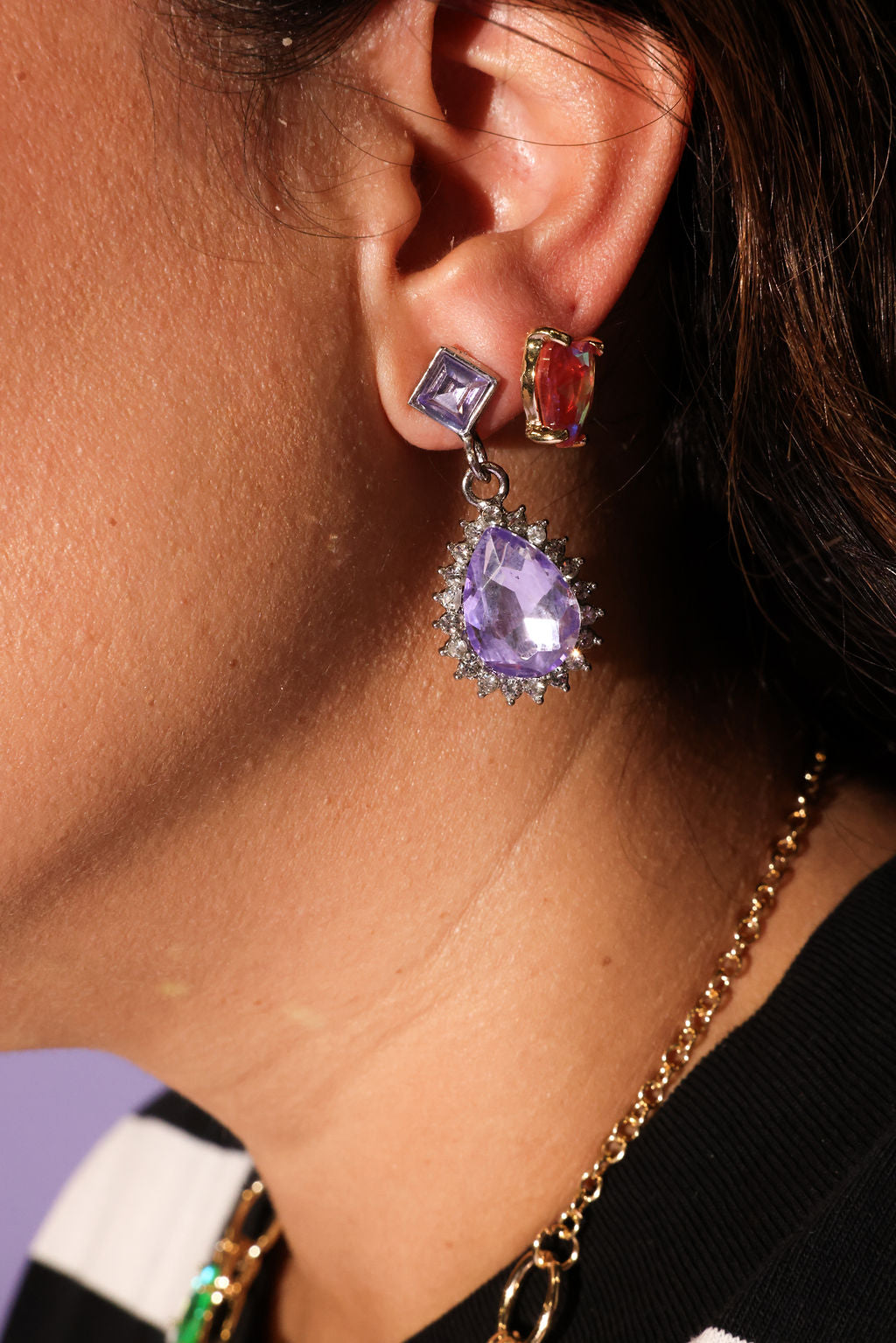 Close-up of an ear wearing a purple teardrop earring with a gold chain necklace