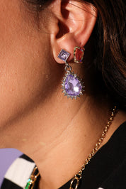 Close-up of an ear wearing a purple teardrop earring with a gold chain necklace