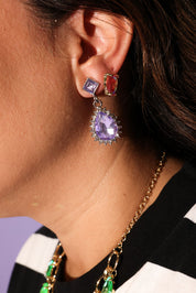 Close-up of a person wearing colorful gemstone earrings and a necklace