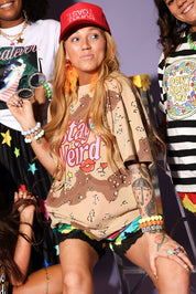 Person wearing a 'Stay Weird' shirt with colorful accessories and tattoos, surrounded by others