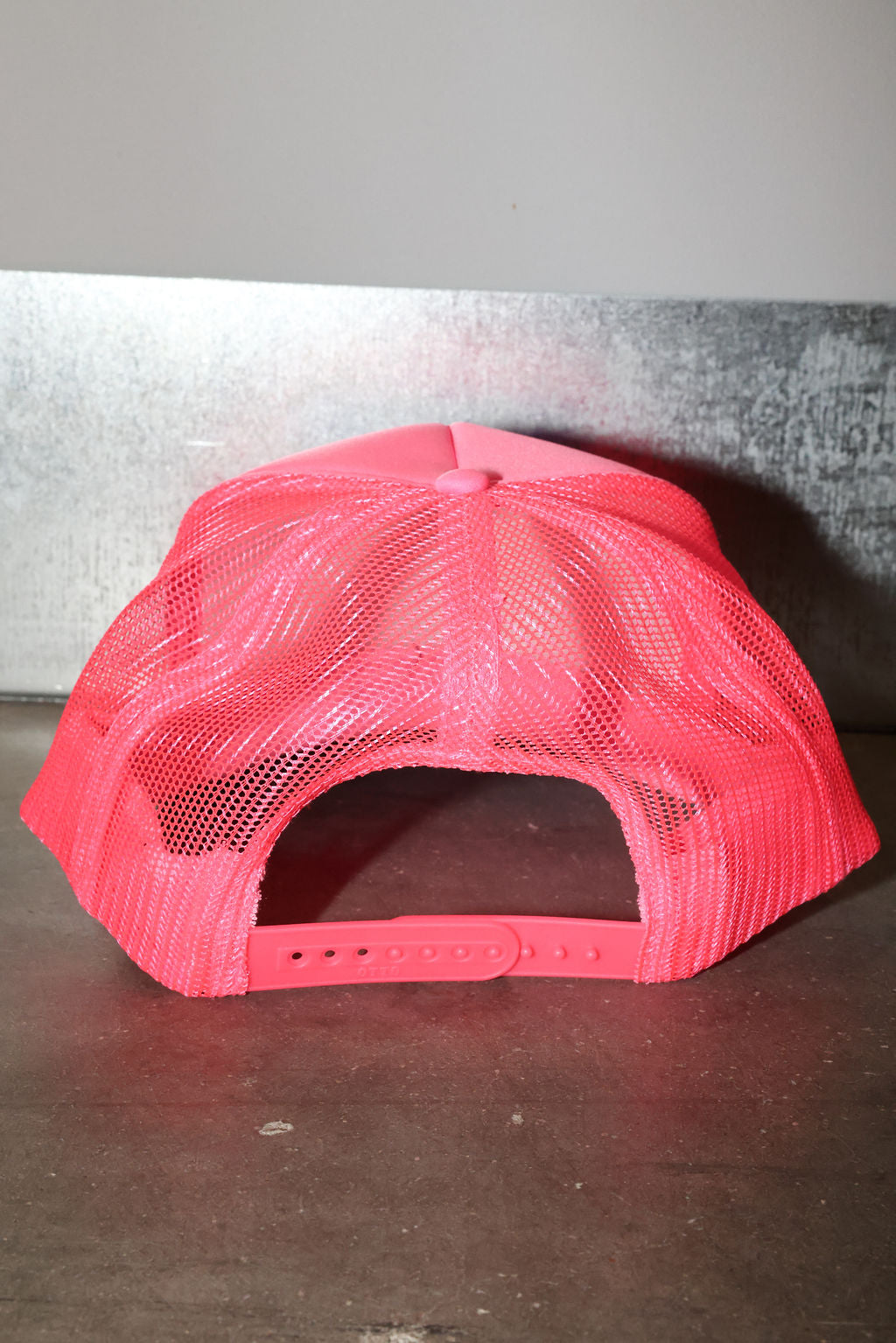 Pink mesh trucker hat on a metallic surface, back view