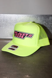 A neon yellow-green trucker hat with mesh back panels and a front patch reading 'I'M JUST A GIRL'. The hat is photographed on a dark surface against a gray wall