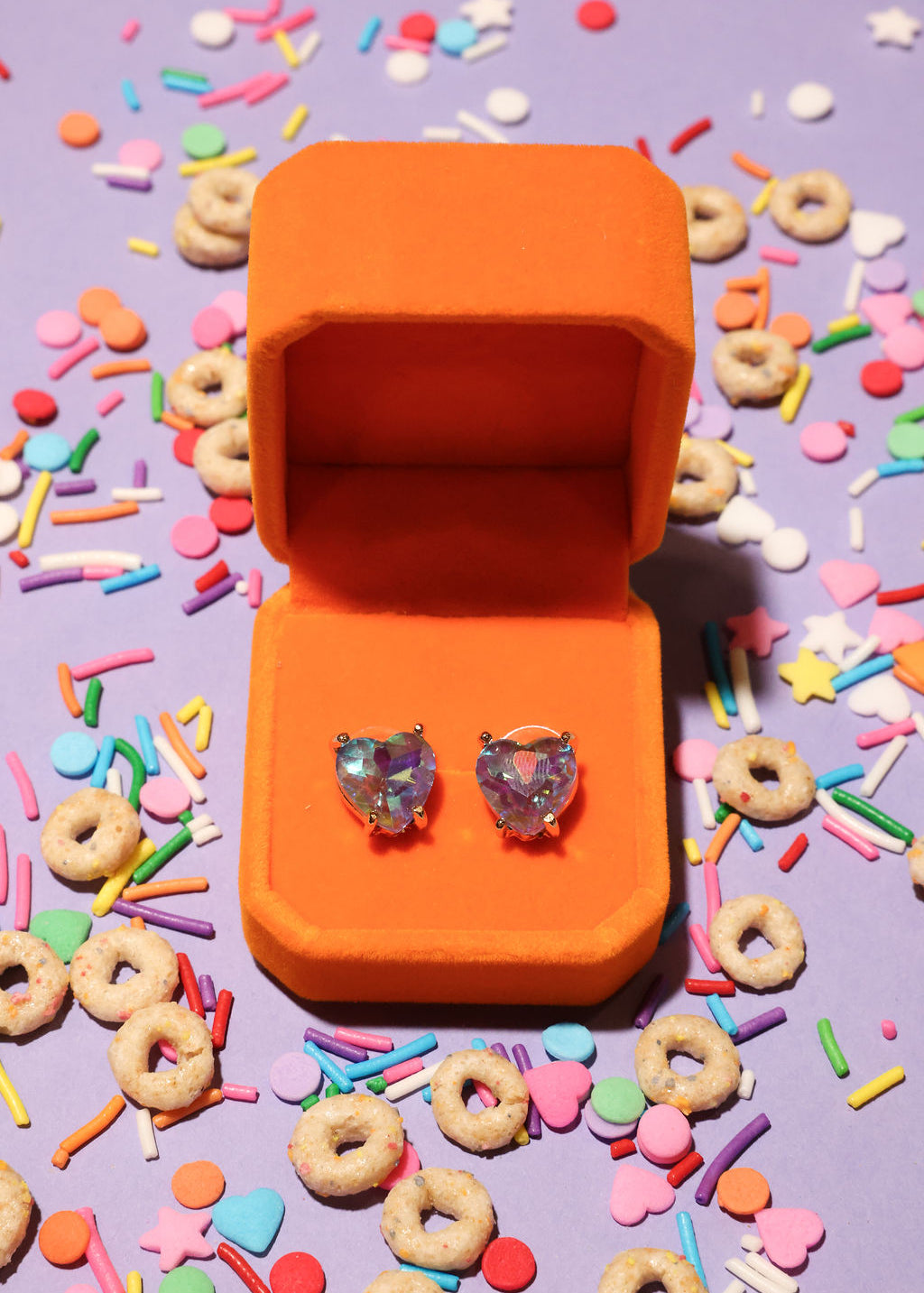 Heart-shaped earrings in an orange box on a colorful candy-themed background