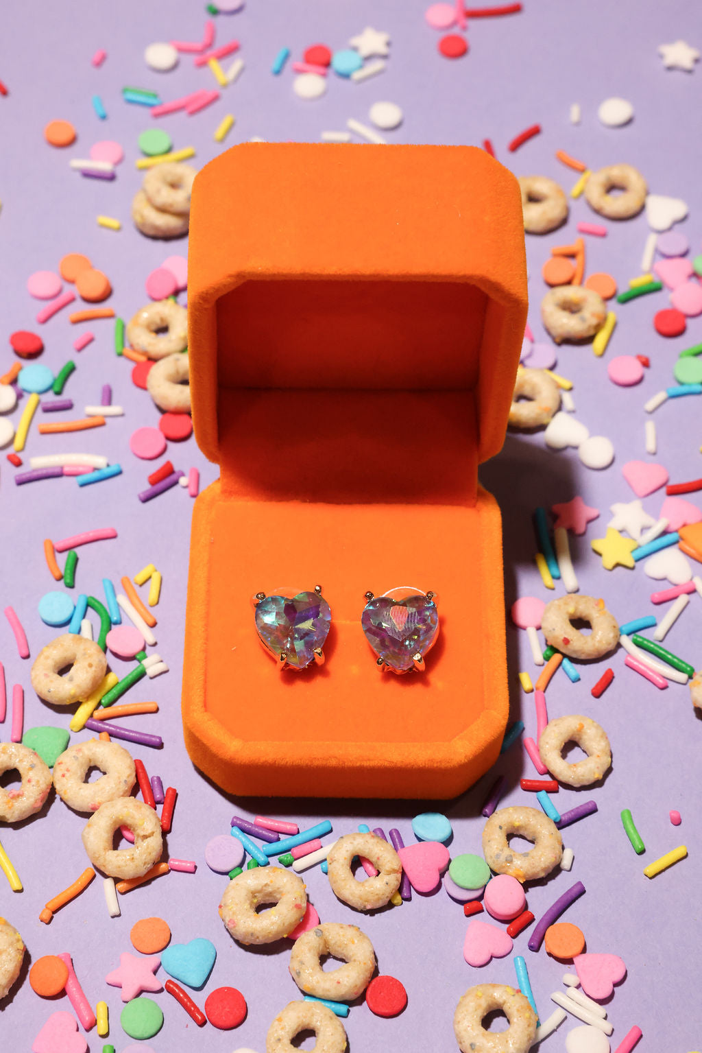Heart-shaped earrings in an orange box on a colorful candy-themed background