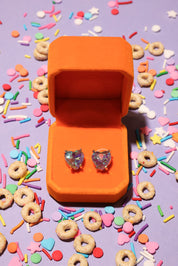 Heart-shaped earrings in an orange box on a colorful candy-themed background