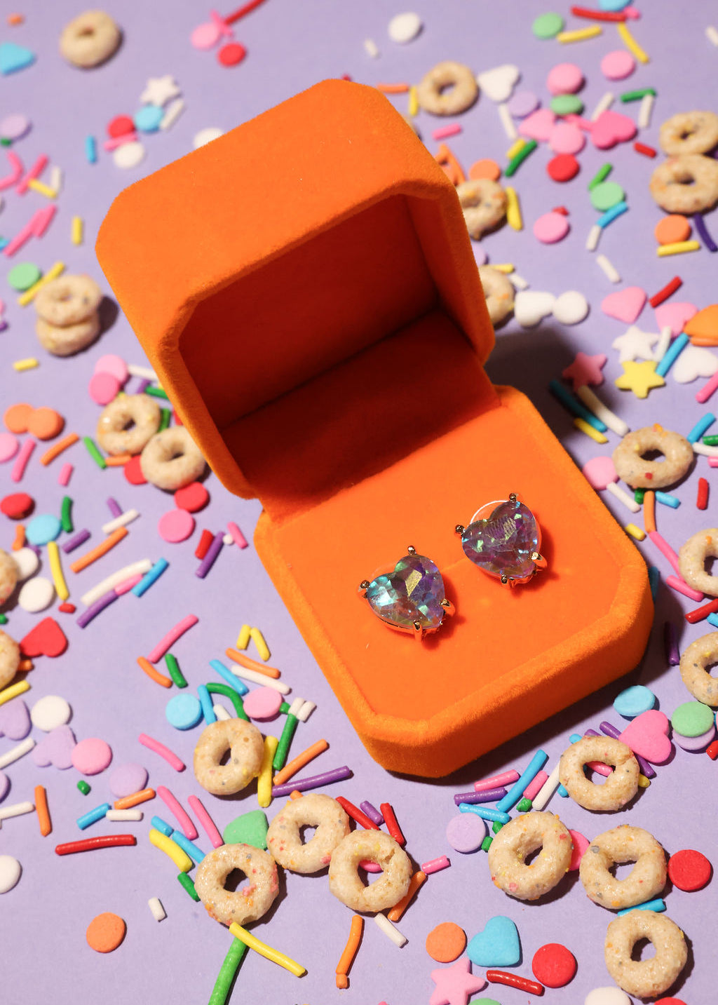 Open orange jewelry box with heart-shaped earrings on a colorful cereal-themed background