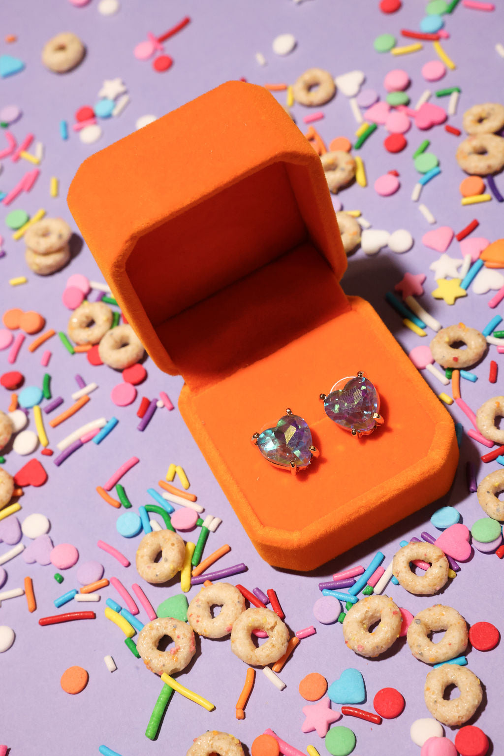 Open orange jewelry box with heart-shaped earrings on a colorful cereal-themed background