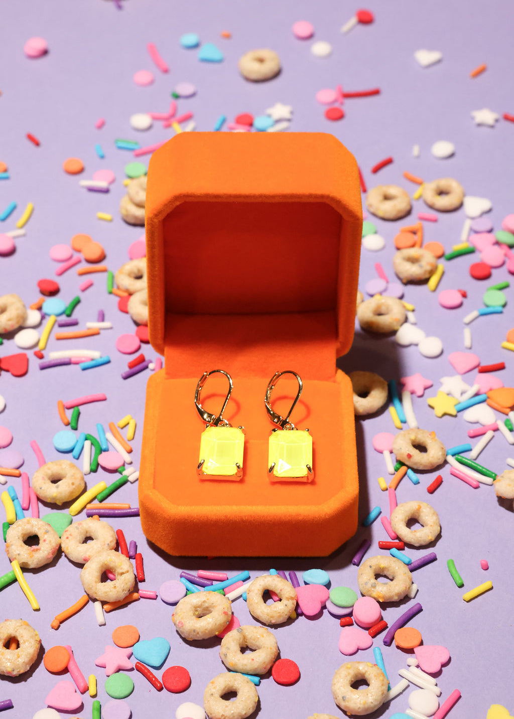 Neon Yellow square-shaped earrings in an orange box on a colorful sprinkles background