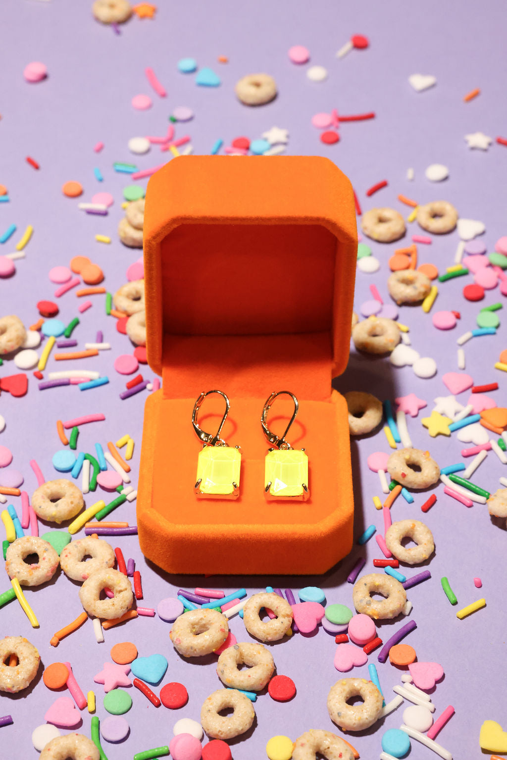 Neon Yellow square-shaped earrings in an orange box on a colorful sprinkles background
