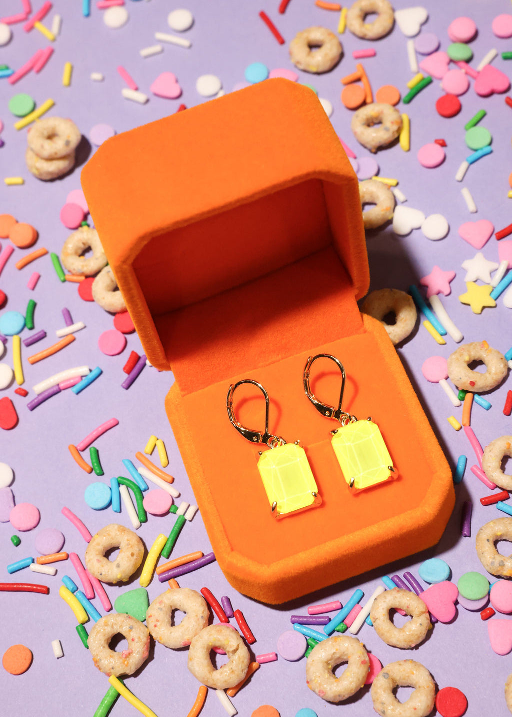 Yellow earrings in an orange box on a colorful sprinkles background