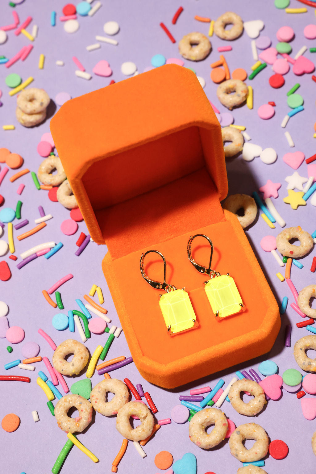 Yellow earrings in an orange box on a colorful sprinkles background