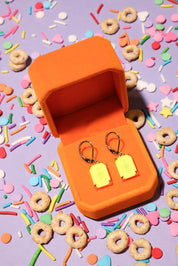 Yellow earrings in an orange box on a colorful sprinkles background