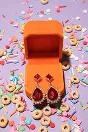 Red earrings in an open orange jewelry box with colorful sprinkles and cereal on a purple background