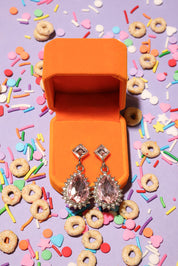 Open orange jewelry box with sparkling earrings on a colorful cereal and sprinkles background