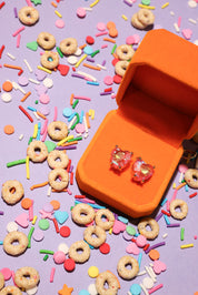 Orange jewelry box with heart-shaped earrings on a colorful sprinkles and cereal background