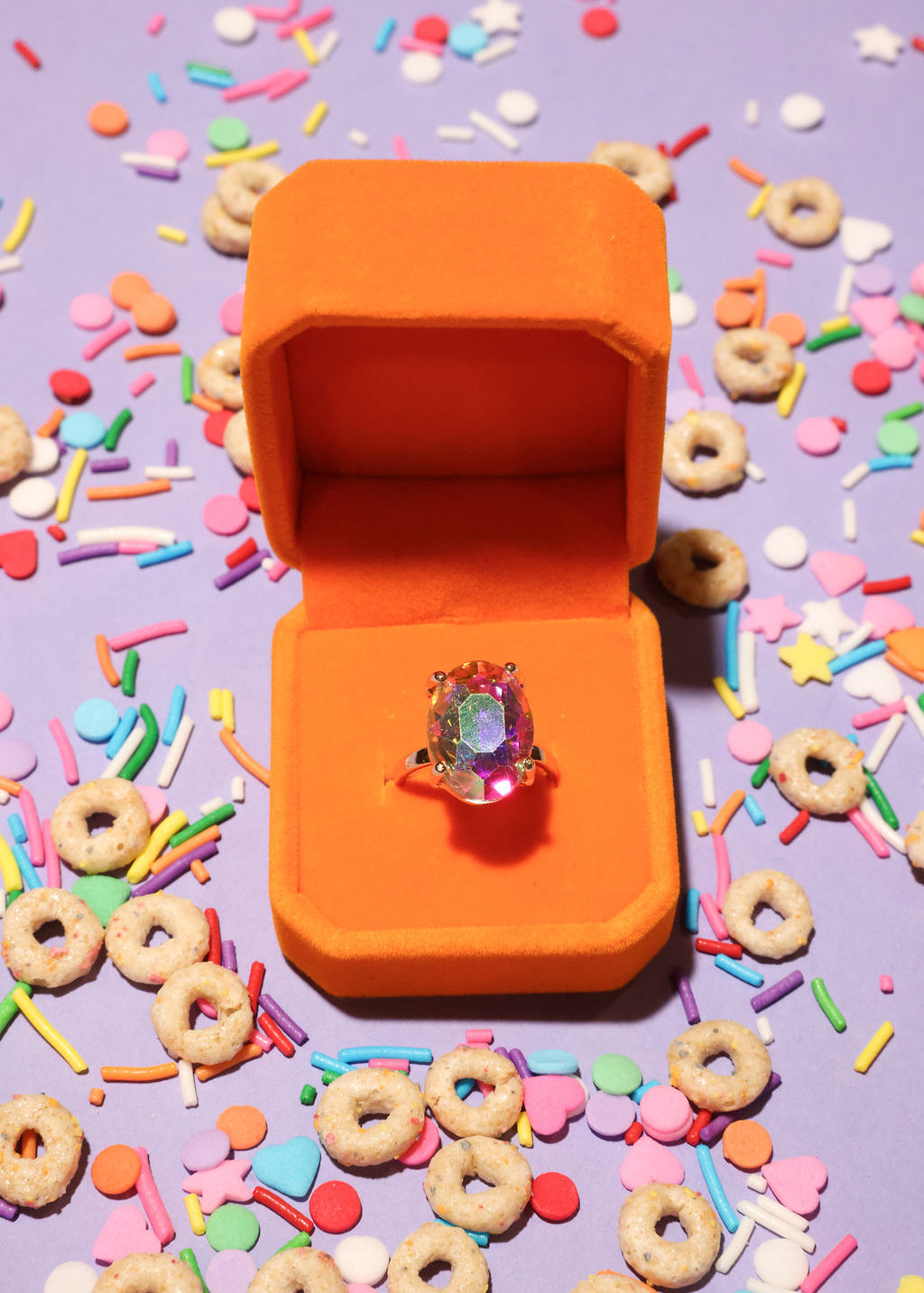 Colorful ring in an orange box surrounded by cereal and sprinkles on a purple background