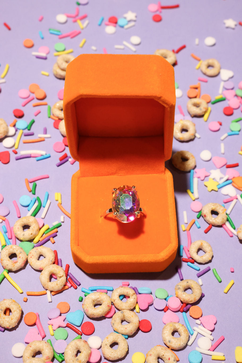 Colorful ring in an orange box surrounded by cereal and sprinkles on a purple background