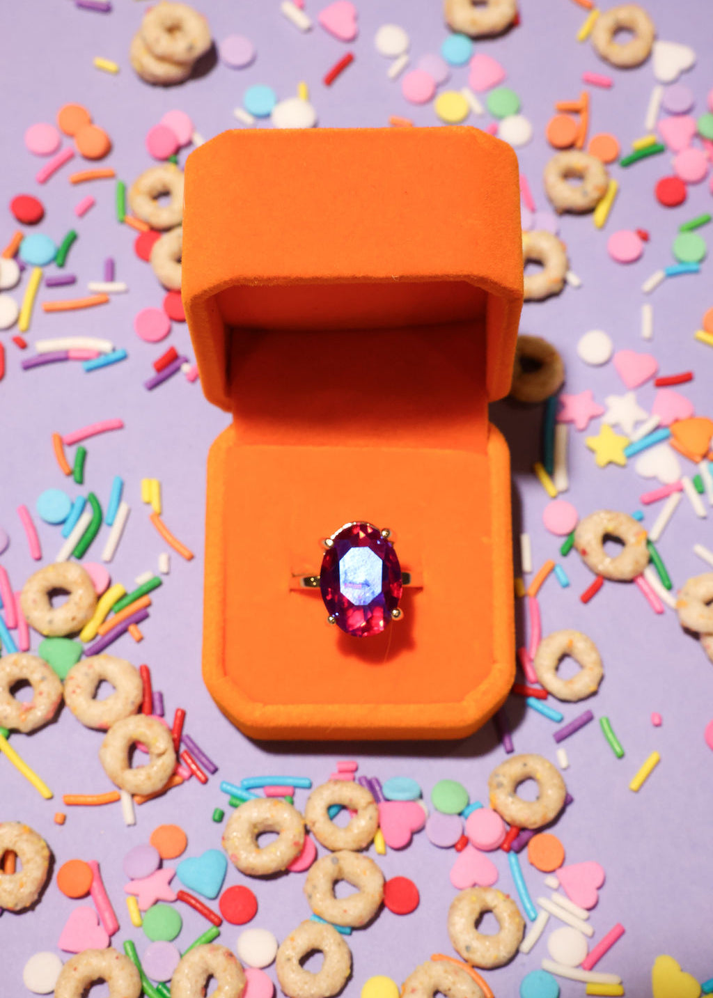 Open orange jewelry box with a ring on a colorful cereal and sprinkles background
