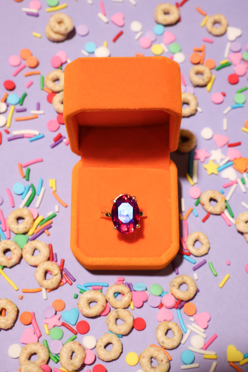 Open orange jewelry box with a ring on a colorful cereal and sprinkles background