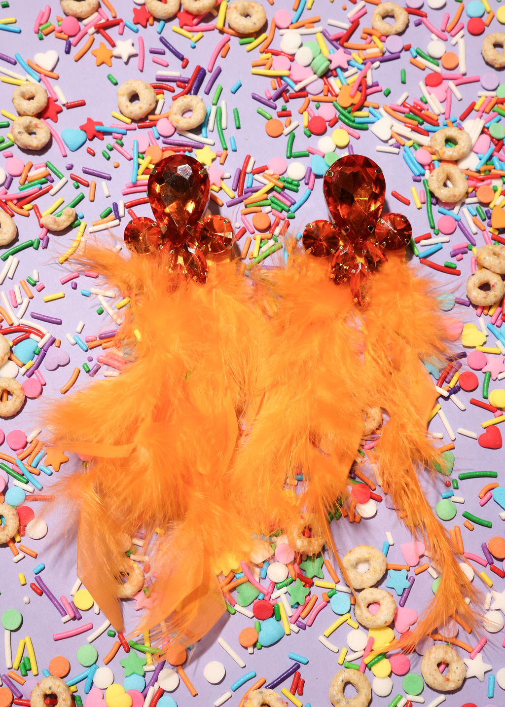 Orange feathered earrings on a colorful sprinkles background