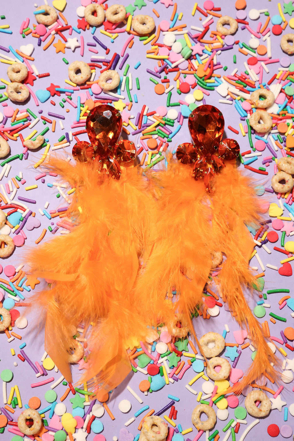 Orange feathered earrings on a colorful sprinkles background