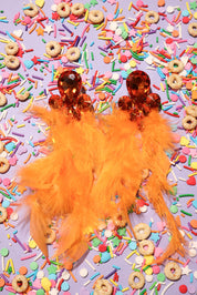 Orange feathered earrings on a colorful sprinkles background