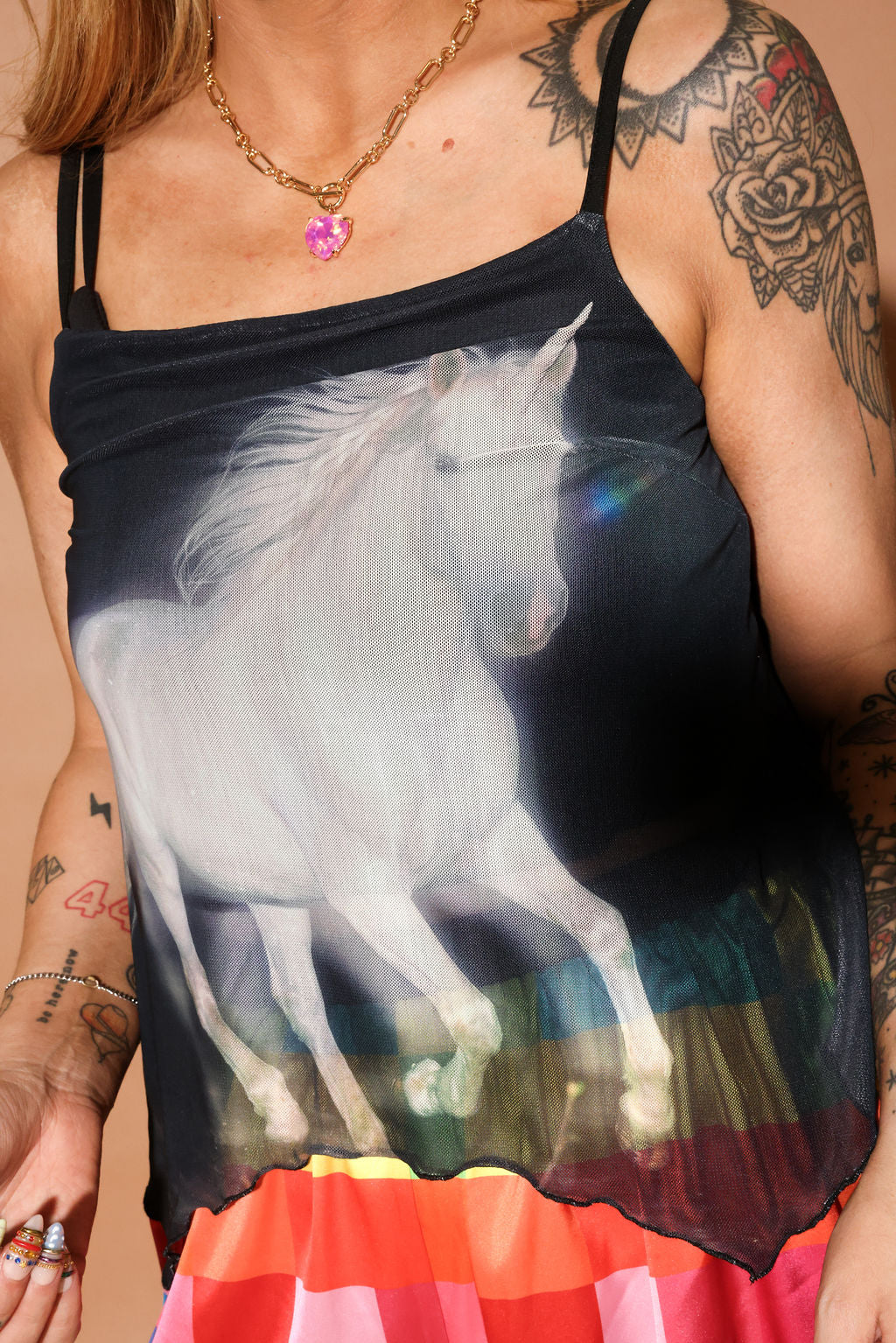 Model wearing a tank top with a unicorn design and colorful skirt, showcasing tattoos on arms, close up view