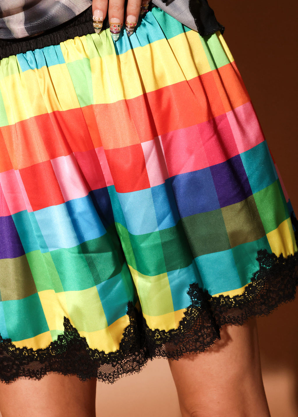 Colorful checkered satin shorties with black lace trim on a plain background, close up view