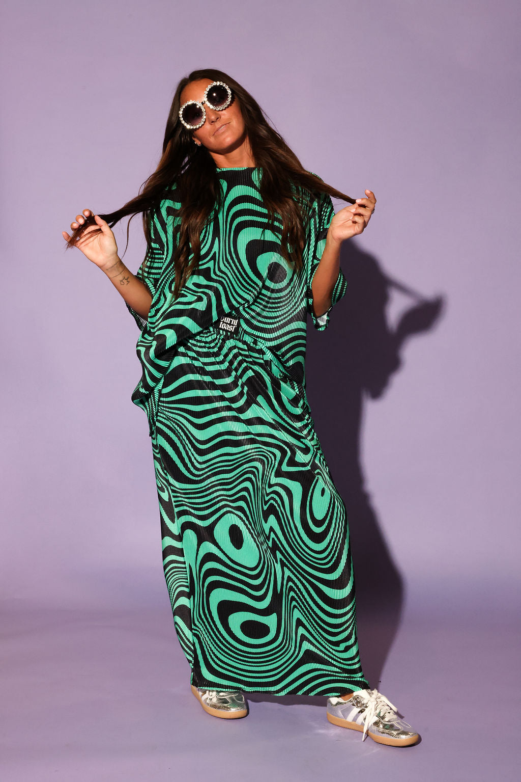 Model wearing a green and black swirl patterned short sleeve and skirt plisse set,  on a purple background, frontal view