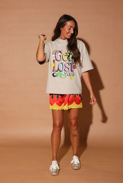 Woman wearing a 'Get Lost' t-shirt and colorful shorts on a beige background, frontal view