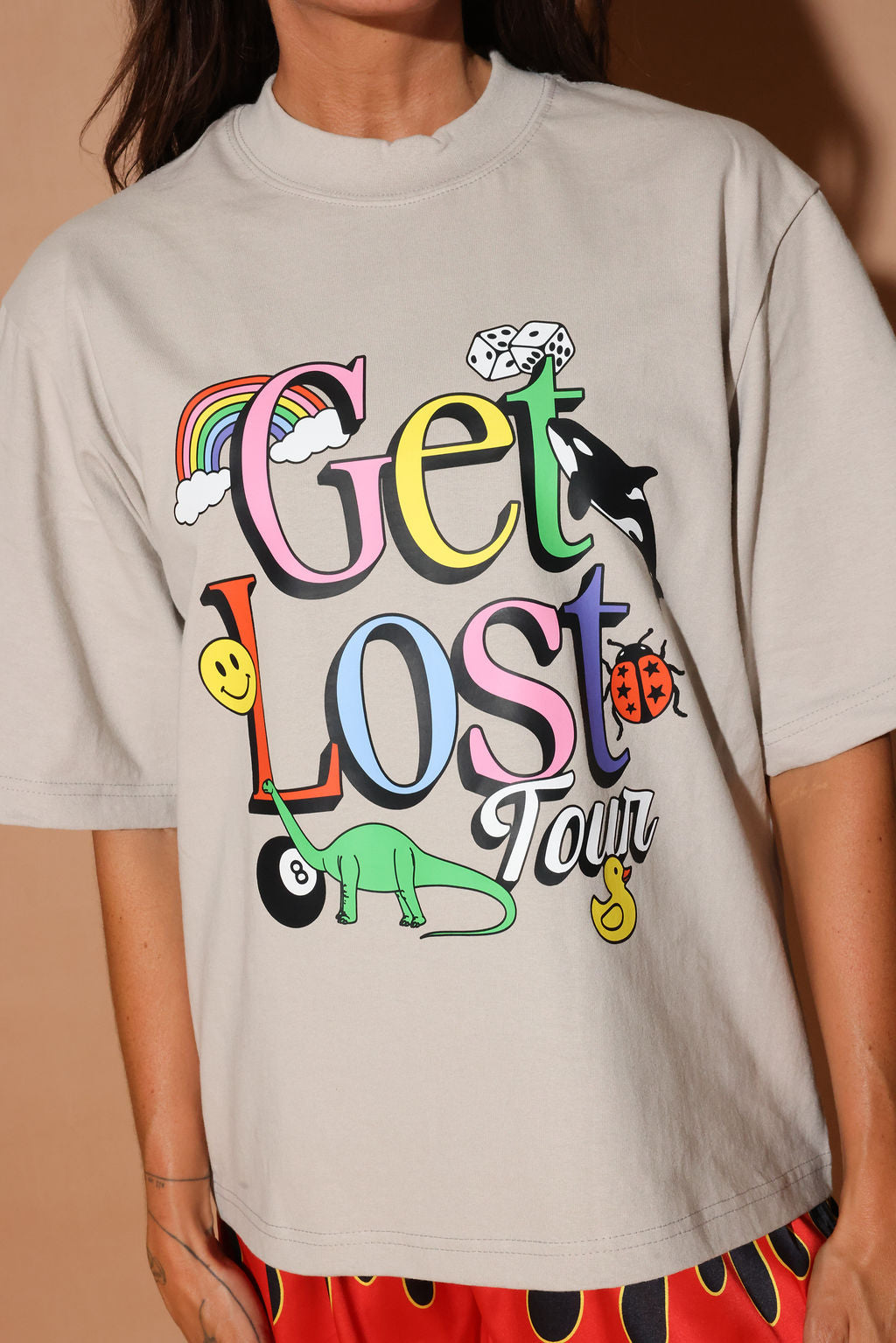Beige t-shirt with colorful graphics and text on a brown background, close up frontal view
