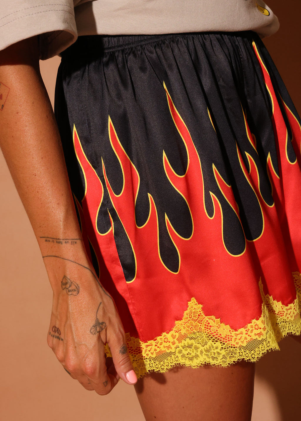 Model wearing a black, red, and yellow flame-patterned shorties with lace trim on a brown background, close up side view
