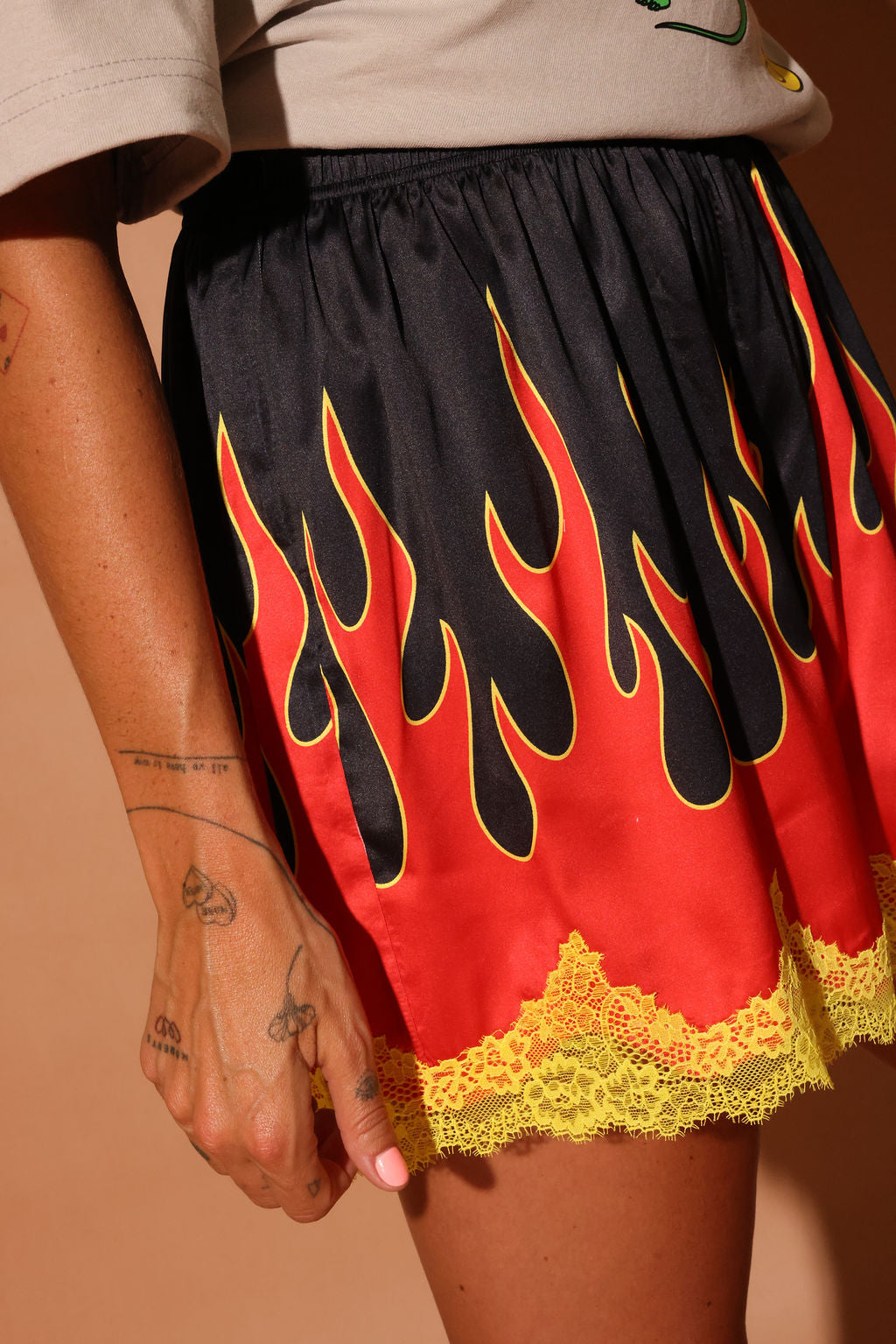 Model wearing a black, red, and yellow flame-patterned shorties with lace trim on a brown background, close up side view