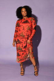 A model with curly black hair in a studio setting against a solid lavender background, wearing a long-sleeve dress in a vibrant orange-red color with a black graphic print, frontal view